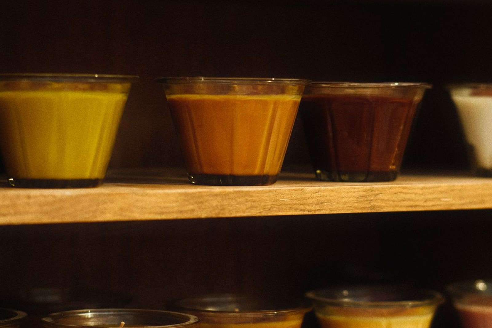 Row of ten identical candles on a stainless bench with batch records and shipping boxes